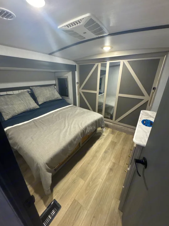 Modern RV rental bedroom: queen bed with grey bedding, overhead AC, and mirrored closets for comfortable travel.. Forest River Salem Hemisphere 2024