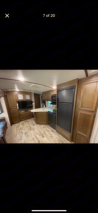 RV rental interior: modern kitchen with island, fridge, and wood-look flooring. Includes a living area.. Keystone RV Cougar 2019