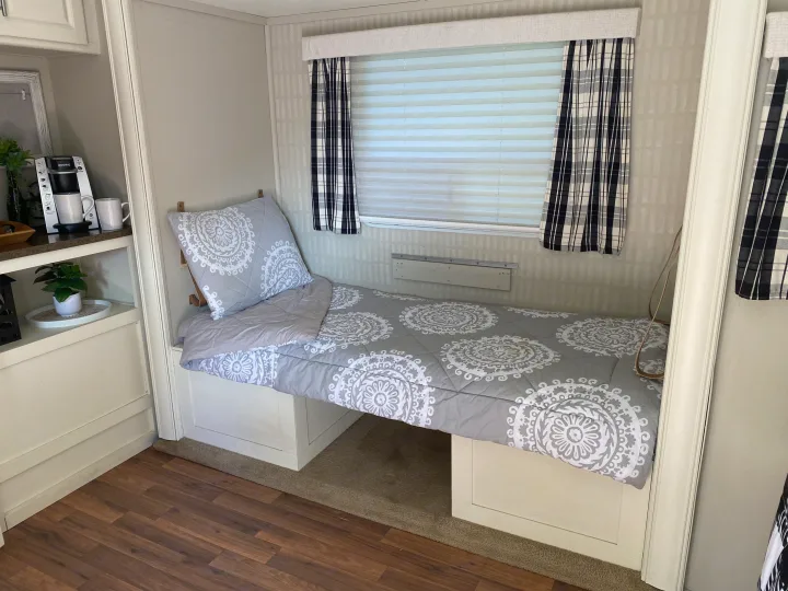 Cozy RV rental interior showing bed with mandala bedding, a window with blinds, and a coffee station.. Cruiser RV Fun Finder X 2011