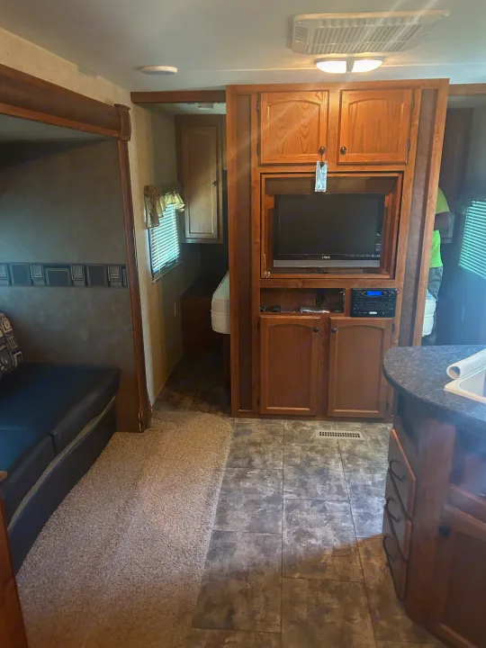 Spacious RV rental interior featuring a living room sofa, entertainment center, kitchen counter, and private bedroom area.. Heartland Trail Runner 2013