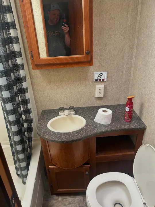 Compact RV rental bathroom with sink, toilet, shower curtain, and mirror reflection of photographer.. Heartland Trail Runner 2013
