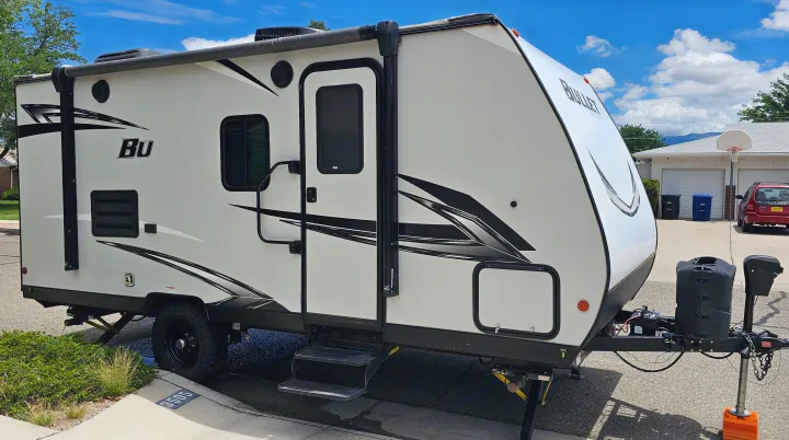 White Bullet travel trailer, ideal for rv rental adventures, parked outside with blue sky. View shows its side, steps, and front hitch.. Keystone RV Bullet Crossfire 2021