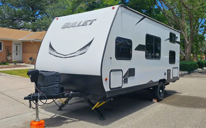 A white Bullet travel trailer for RV rental, parked on pavement with stabilizer jacks down, ready for your next adventure.. Keystone RV Bullet Crossfire 2021