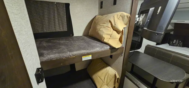 RV rental bunk room: upper bed with grey blanket, lower sleeping area, and a dinette with a mounted TV. Efficient use of space.. Keystone RV Bullet Crossfire 2021