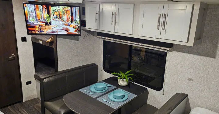 Inside an RV rental: Dinette with place settings, large TV over bunk beds, window, and light grey cabinets.. Keystone RV Bullet Crossfire 2021