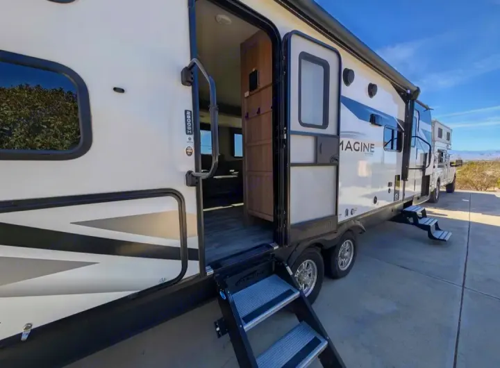 This RV rental features an open travel trailer with steps, ready for an adventure in a sunny, desert landscape.. Grand Design Imagine 2022