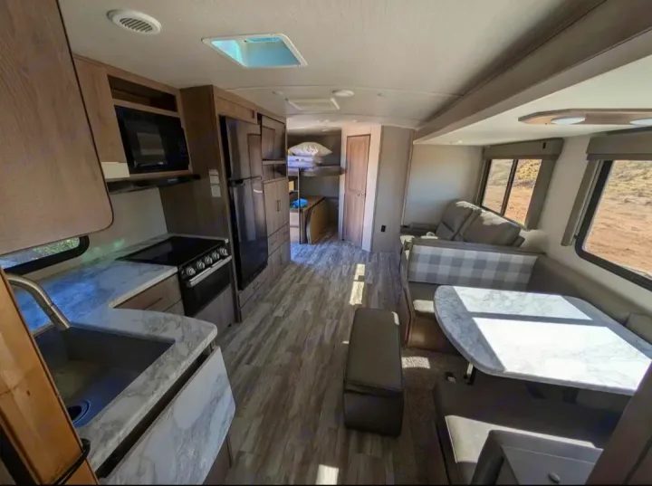 Bright rv rental interior showcasing a kitchen with microwave, stove, fridge, dinette, sofa, and bunk beds.. Grand Design Imagine 2022