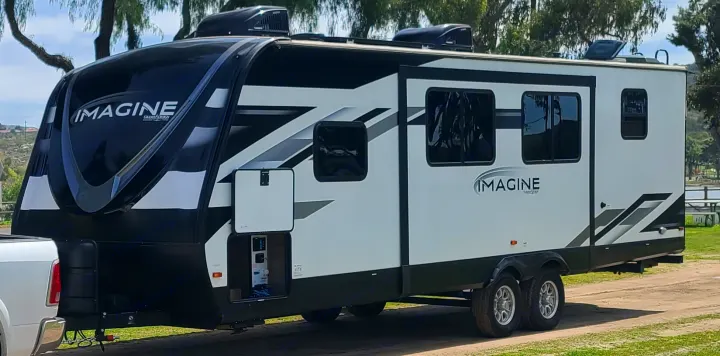 A striking black and white Grand Design Imagine travel trailer, perfect as an RV rental, is set up for outdoor adventures.. Grand Design Imagine 2022