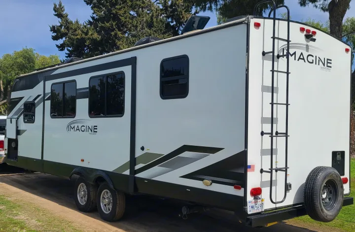 A white Grand Design Imagine recreational vehicle (RV), typical for an RV rental, is parked outdoors, ready for travel.. Grand Design Imagine 2022