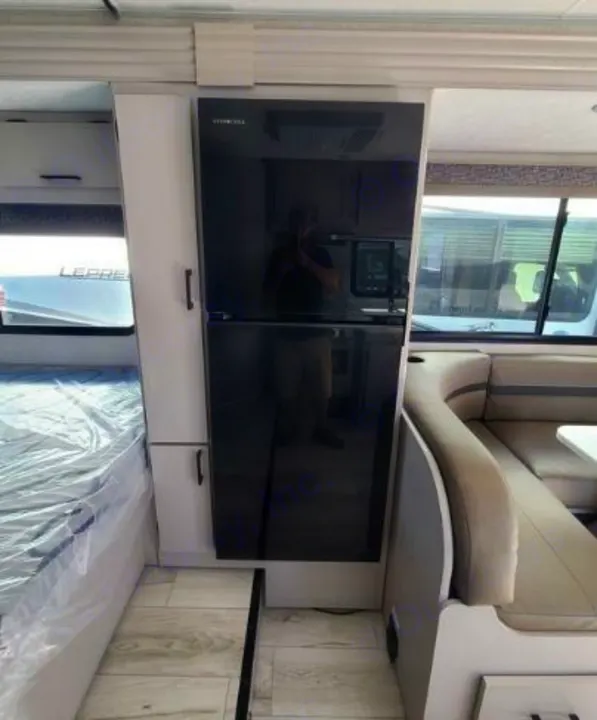 Inside an RV rental: modern black refrigerator, cozy bed, and dinette seating. Ready for travel adventures.. Forest River Coachmen Freelander 2025