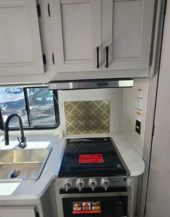 RV rental kitchen: light cabinets, window, modern stove/oven, sink, and stylish backsplash.. Forest River Coachmen Freelander 2025