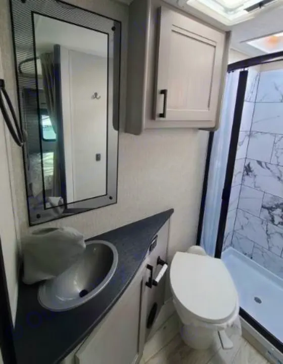 Modern RV rental bathroom featuring a sink, toilet, mirror, and marble-tiled shower, offering a clean, compact space.. Forest River Coachmen Freelander 2025