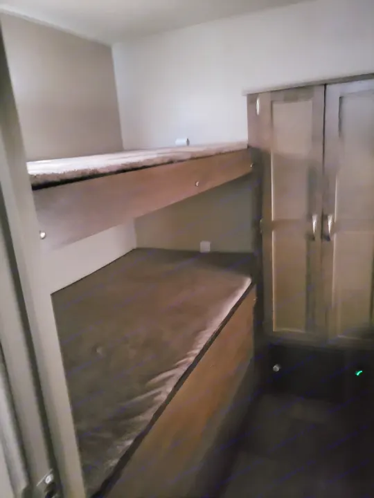 An RV rental's compact interior features two stacked bunk beds with soft mattresses and a tall wooden cabinet on the right.. Forest River Palomino Puma 2018