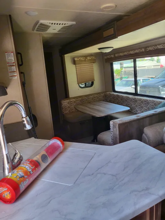 RV rental interior: kitchen with a sink, countertop, and a dinette booth. Ready for travel or mobile living.. Forest River Palomino Puma 2018
