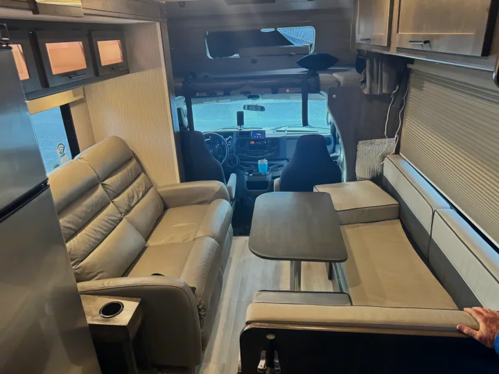 RV rental interior: spacious living area with light-toned sofa, dinette, and driver's cabin with overhead bunk.. Forest River Coachmen Leprechaun Premier 2022