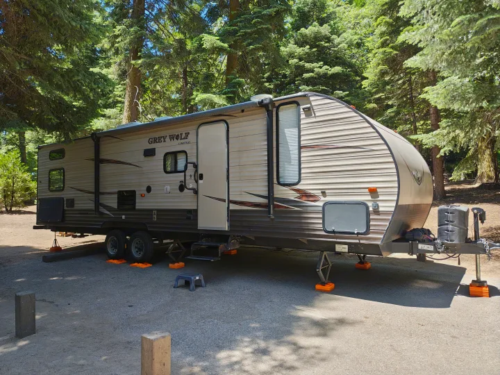 Grey Wolf travel trailer parked at a serene campsite among tall trees, ready for your next RV rental adventure.. Forest River Cherokee Grey Wolf 2016