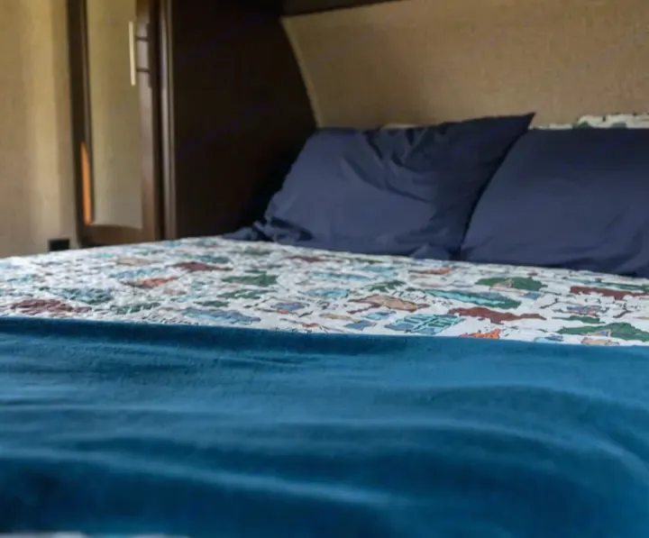 Low angle view of an RV rental bedroom with a bed featuring a patterned quilt, dark blue pillows, and a teal blanket.. Forest River Cherokee Grey Wolf 2016