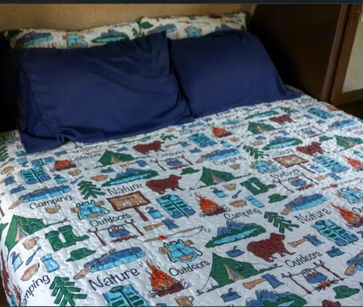 Cozy RV rental bed with camping-themed quilt and navy pillows, featuring tents, bears, and "Nature" text.. Forest River Cherokee Grey Wolf 2016