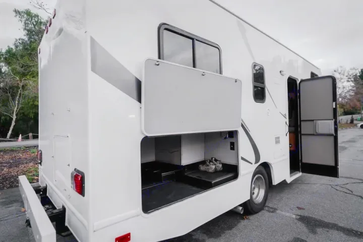 White RV rental with open side storage compartments & entry door, revealing ample space for travel gear.. Thor Majestic 2017