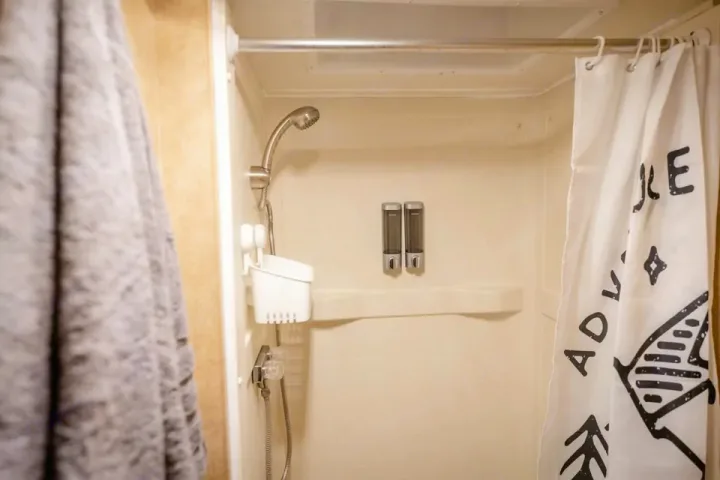 Clean RV rental shower with handheld head, wall dispensers, and an "ADVENTURE" curtain, ideal for your travels.. Thor Majestic 2017
