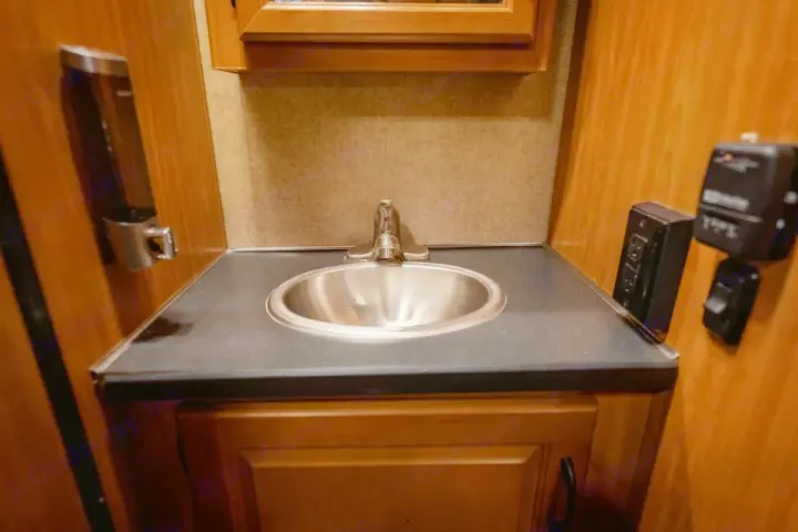 Explore an RV rental's compact bathroom: stainless steel sink, faucet, and essential wall controls on a dark counter.. Thor Majestic 2017
