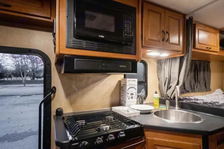 RV rental interior with a compact kitchen featuring a stove, sink, microwave, and overhead cabinets, plus a sleeping area.. Thor Majestic 2017