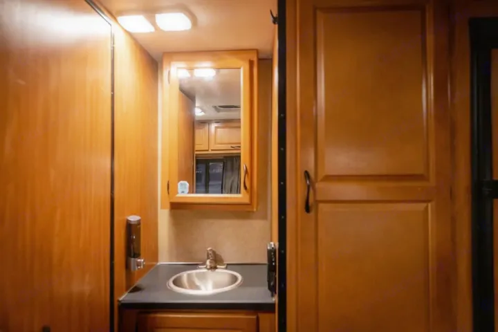 Compact RV rental bathroom interior featuring a wood vanity, sink, mirror, and overhead lighting.. Thor Majestic 2017