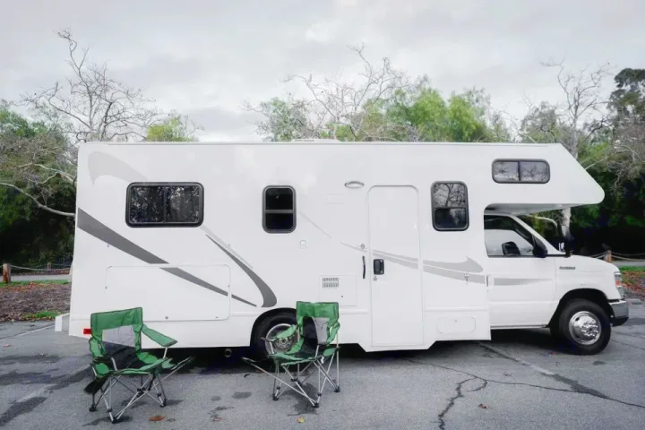 White RV rental with two green chairs parked on asphalt, ready for a comfortable camping adventure.. Thor Majestic 2017