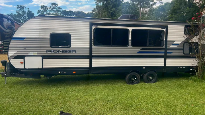 A grey & white Pioneer travel trailer (RV) on grass, ideal for RV rental & camping trips.. Heartland RVs Pioneer 2023