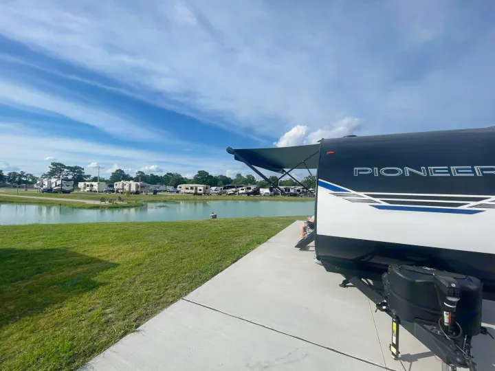 Scenic RV rental: Pioneer travel trailer parked lakeside at a sunny campground. Ideal for relaxing getaways.. Heartland RVs Pioneer 2023