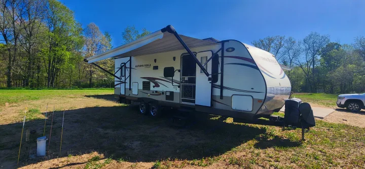 Beige Autumn Ridge travel trailer with extended awning, parked in a sunny, grassy field. Great for an RV rental experience.. Starcraft Autumn Ridge 2014