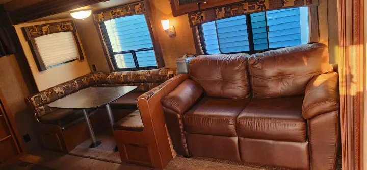 Cozy RV rental interior showing a comfortable brown sofa, U-shaped dinette booth, and windows.. Starcraft Autumn Ridge 2014