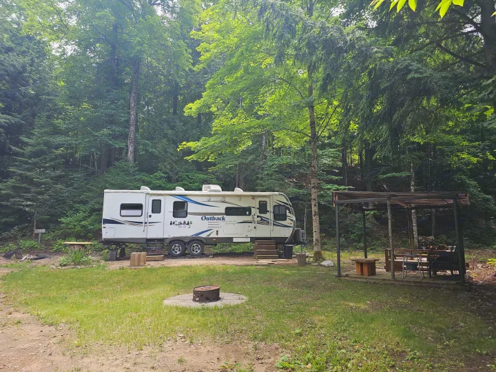 Experience nature with this RV rental parked at a lush, treed campsite, featuring a fire pit and covered patio.. Keystone RV Outback 2013