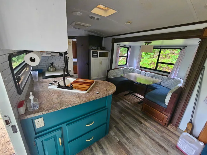 RV rental interior: A modern kitchen with teal cabinets, wood floors, and a bright dining area with outdoor views.. Keystone RV Outback 2013