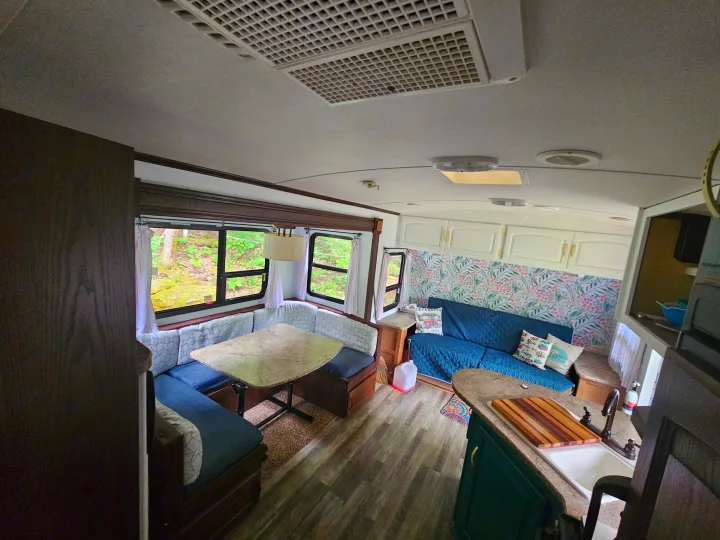 Spacious RV rental interior featuring a U-shaped dinette, sofa, and kitchen, with views of lush greenery.. Keystone RV Outback 2013