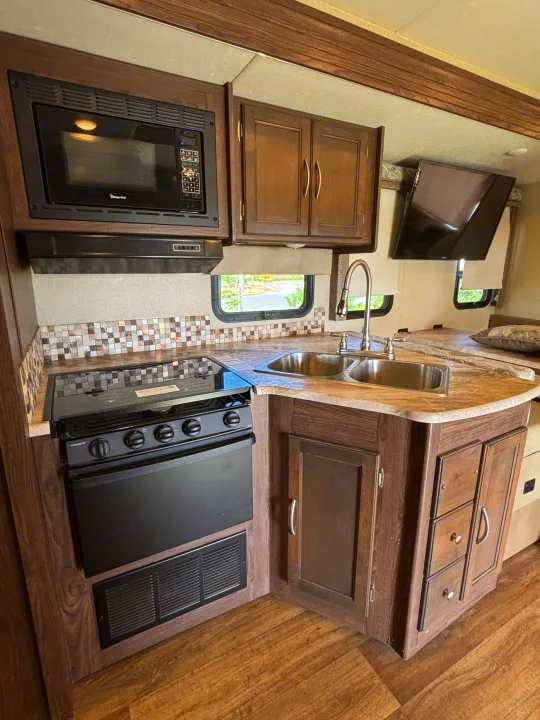 RV rental kitchen: microwave, oven, sink, and TV in a cozy, functional setup for your trips.. Coachmen pursuit Precision 27ds 2019