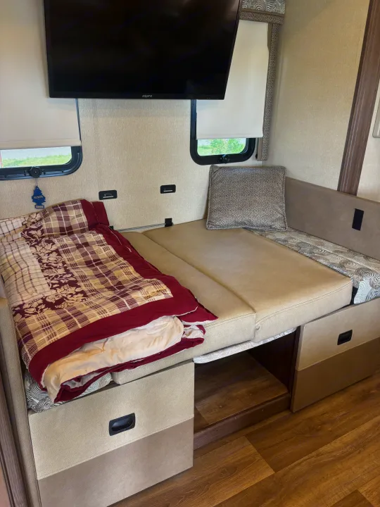 RV rental interior: Dinette converted to a bed with a blanket, mounted TV, and window; shows storage and flooring.. Coachmen pursuit Precision 27ds 2019