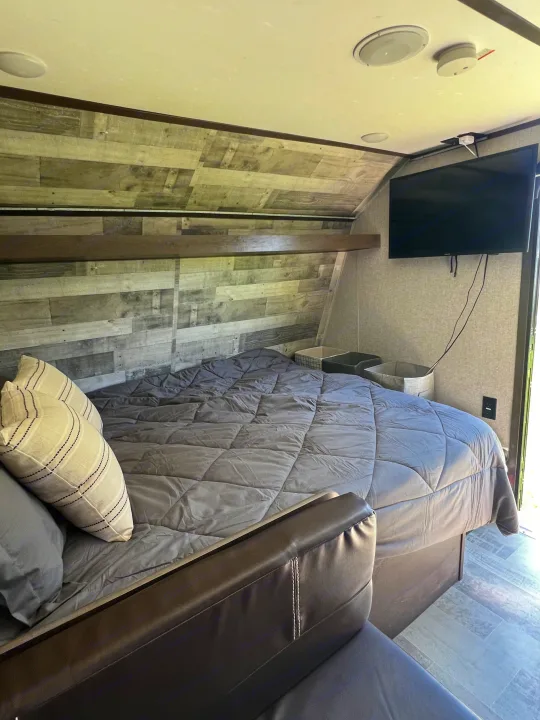 RV rental bedroom: Features a comfy bed with gray comforter, wall-mounted TV, and a stylish wood-planked accent wall.. Dutchmen Coleman Lantern LT 2021