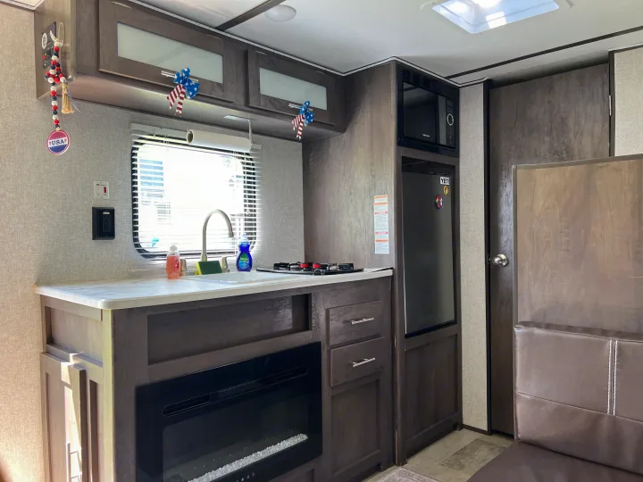 Interior of a modern **rv rental** kitchen featuring a sink, stove, microwave, refrigerator, and an electric fireplace.. Dutchmen Coleman Lantern LT 2021