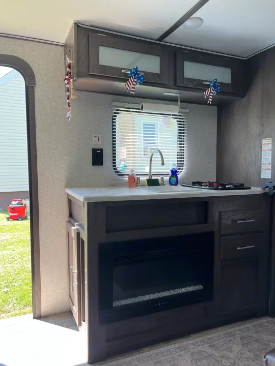 Inside an RV rental: a modern kitchen featuring a sink, gas stove, and electric fireplace. Perfect for your next adventure.. Dutchmen Coleman Lantern LT 2021