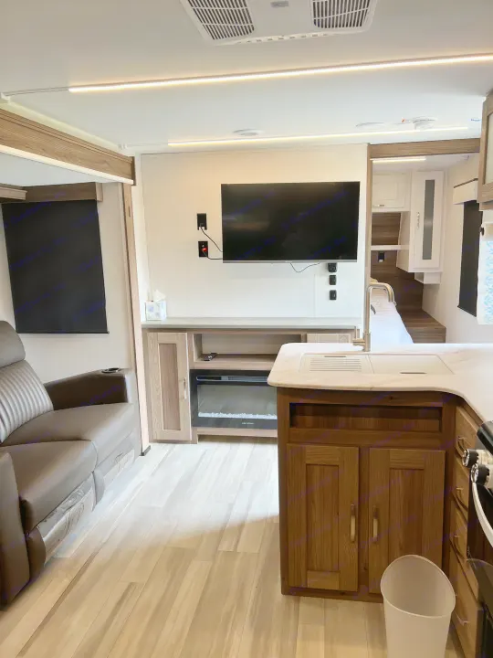 Spacious and modern RV rental interior with a living area, TV, electric fireplace, kitchen, and cozy bedroom space.. Cruiser RV x252 Go Explore 2025