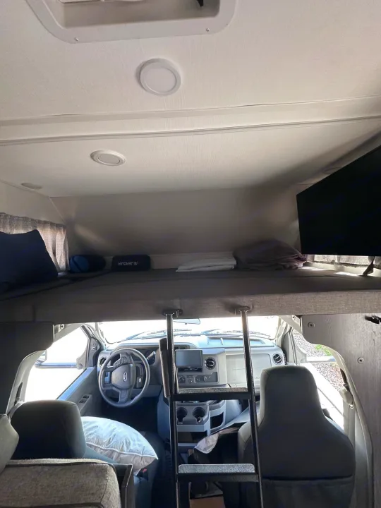 RV rental interior showing over-cab bunk bed, driver's cab, TV, and ladder. Ready for travel!. Forest River Sunseeker Classic 2021