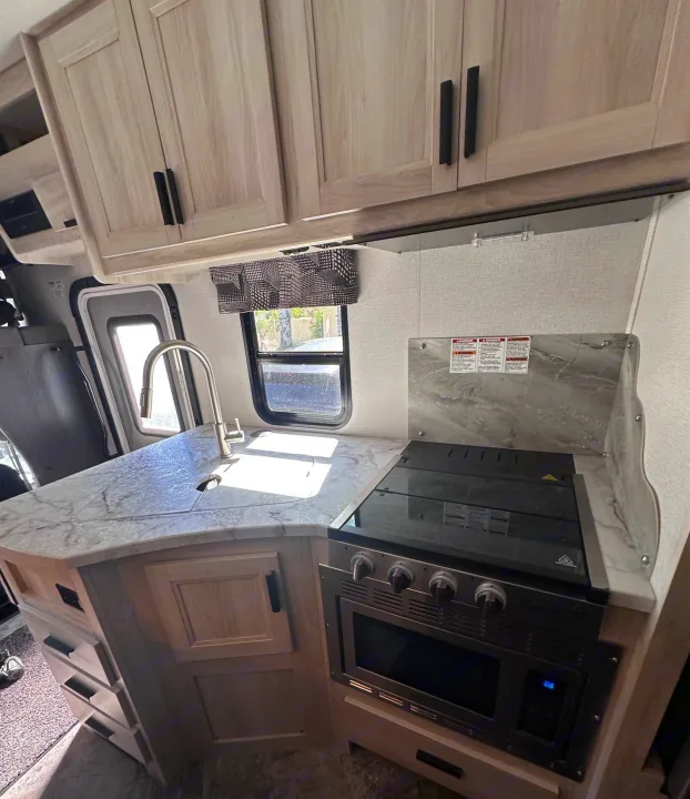 Modern RV rental kitchen featuring light wood cabinets, a marble-patterned counter, sink, and cooking appliances.. Forest River Sunseeker Classic 2021