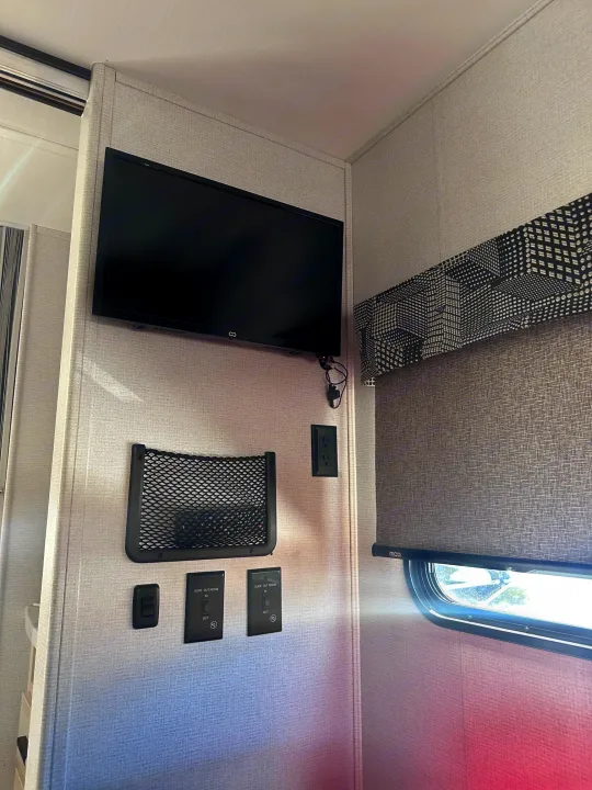 RV rental interior: Mounted TV, storage net, power outlets, slide-out controls, and window with patterned valance.. Forest River Sunseeker Classic 2021