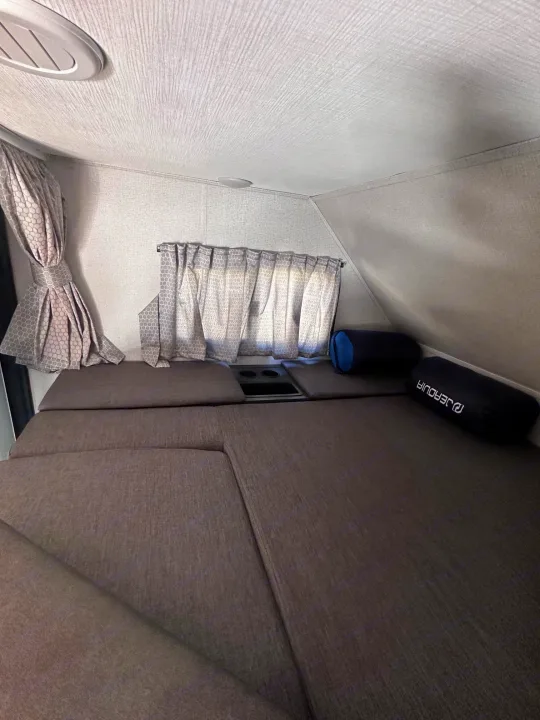 Inside a cozy RV rental: a compact sleeping area with dark grey cushions, patterned curtains, and overhead features.. Forest River Sunseeker Classic 2021