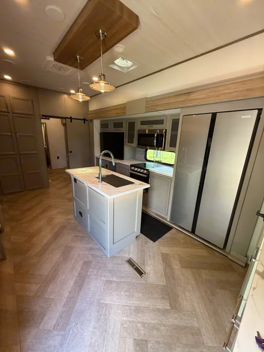 Modern RV rental interior with a spacious kitchen island, stainless steel appliances, and stylish herringbone flooring.. Keystone Sprinter Wide Body 2025
