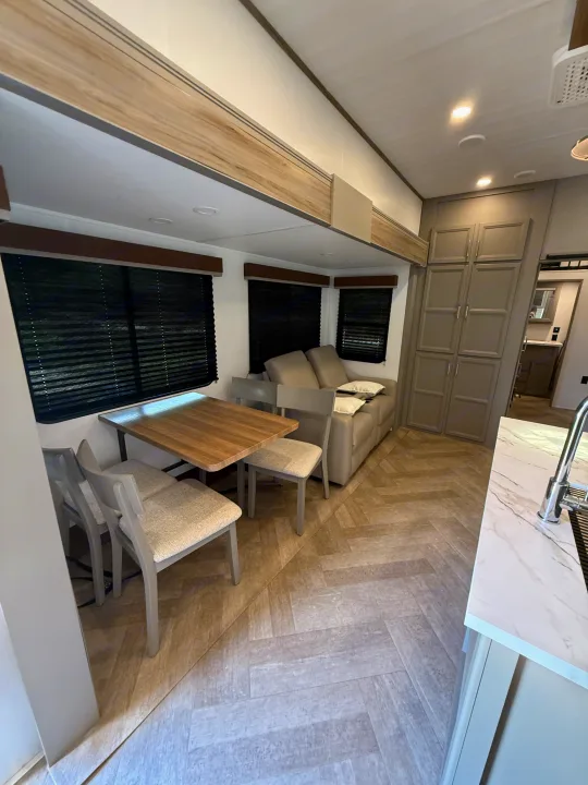 Modern RV rental interior showing a dining table, sofa, gray cabinets, and herringbone flooring.. Keystone Sprinter Wide Body 2025