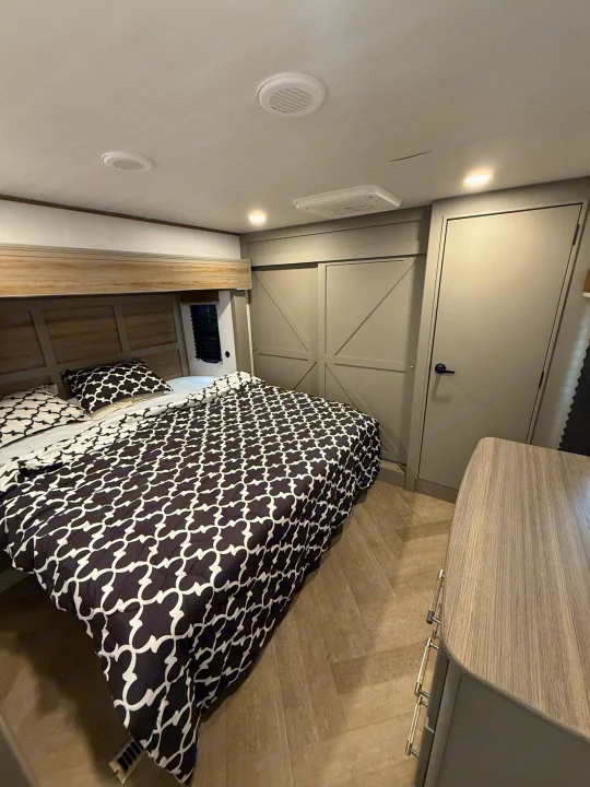 Cozy RV rental bedroom featuring a patterned bed, modern storage, and light wood flooring.. Keystone Sprinter Wide Body 2025