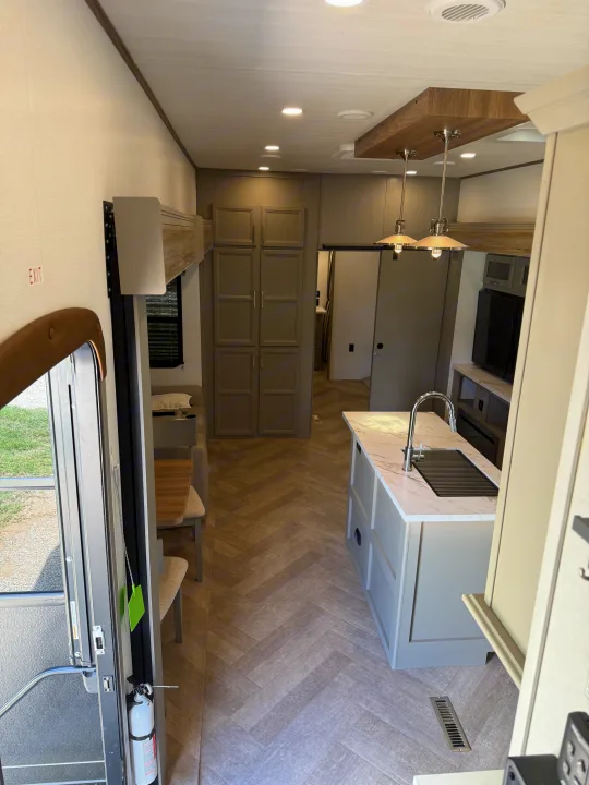 Bright, modern RV rental interior with full kitchen island, dining area, and herringbone floors.. Keystone Sprinter Wide Body 2025