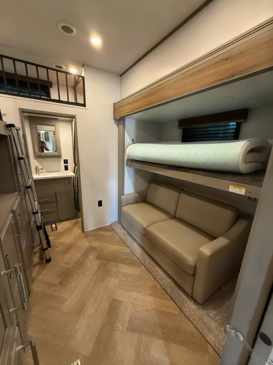 Explore this modern RV rental interior featuring a bunk bed with sofa, bathroom vanity, and loft area, designed for compact living.. Keystone Sprinter Wide Body 2025